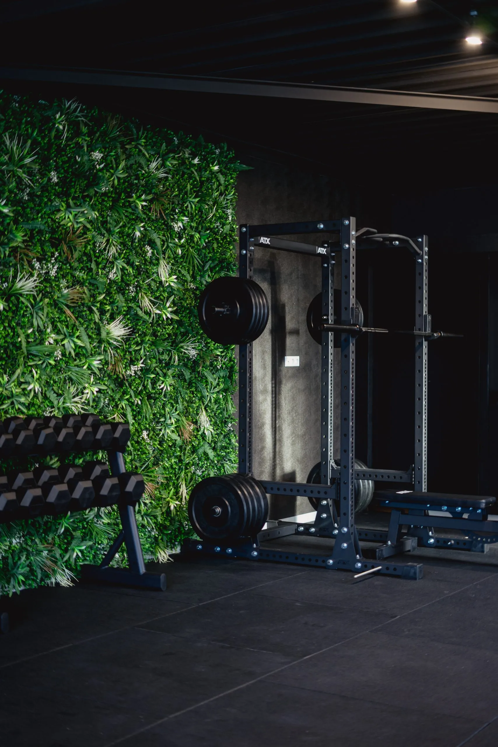 Squatrack en dumbbellrek bij de plantenwand in de privé gym