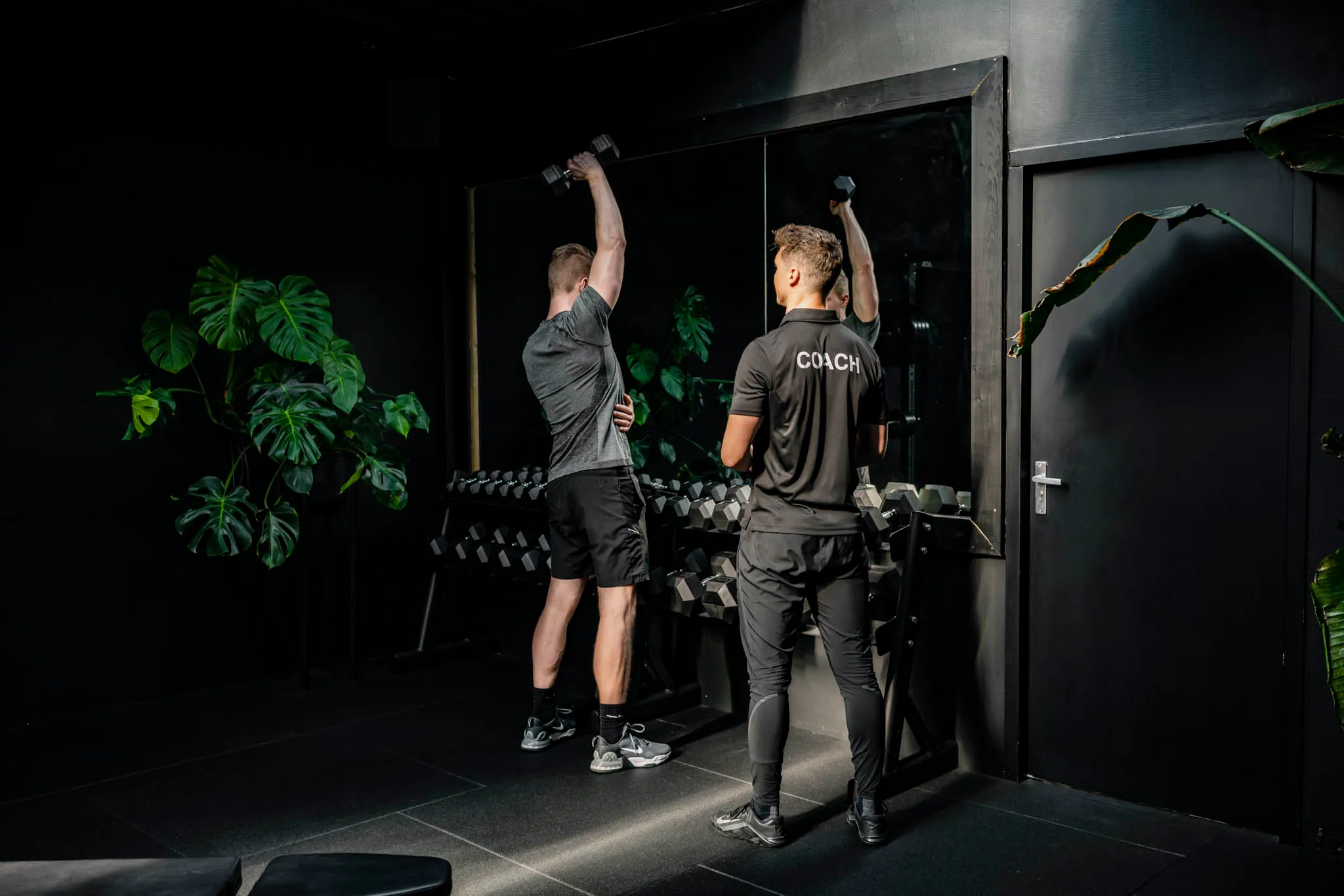 Coach begeleidt een klant bij een schouderdruk-oefening